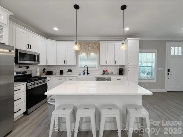 a kitchen with stainless steel appliances granite countertop a sink a stove a refrigerator and white cabinets with wooden floor