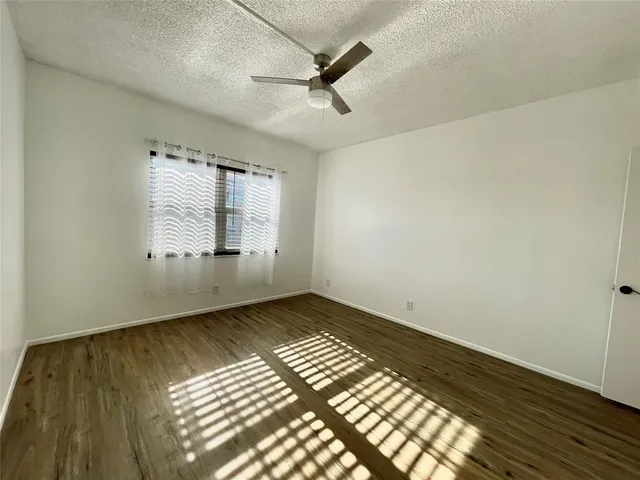 an empty room with wooden floor fan and windows