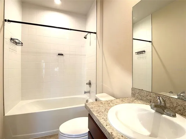 a bathroom with a granite countertop bathtub shower sink vanity and toilet