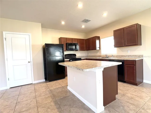 a kitchen with kitchen island granite countertop a stove a refrigerator a sink a microwave and island