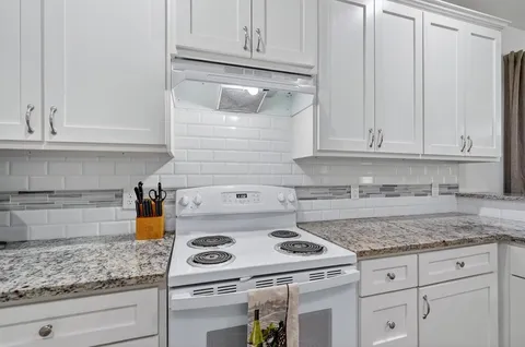 a kitchen with granite countertop white cabinets and a stove