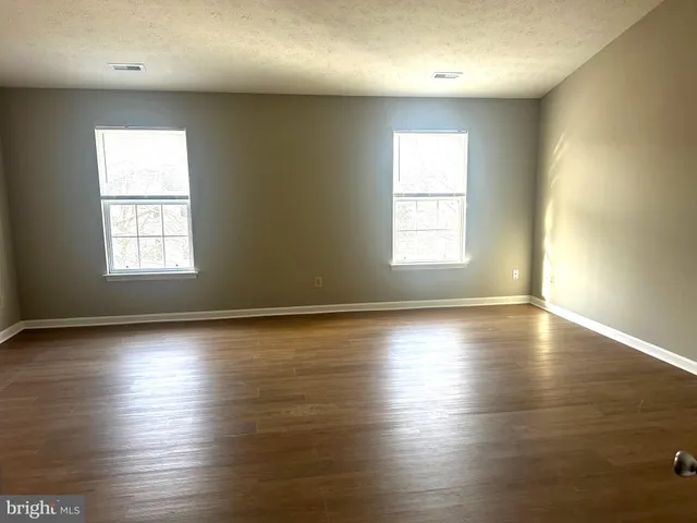 an empty room with wooden floor and windows with curtains