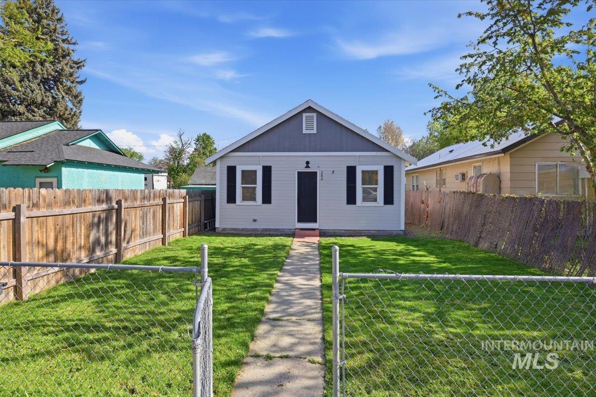284 Fargo Avenue Notus, ID 83656 - Photo 1 of 24 Single-story residence featuring a light gray facade with dark gray gable siding, a central walkway, a chain link front fence, and a wooden perimeter fence
