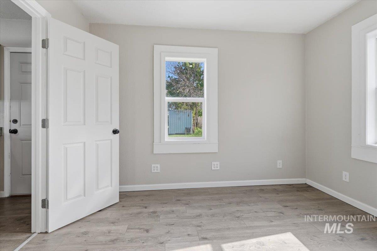 284 Fargo Avenue Notus, ID 83656 - Photo 11 of 24 Bright interior room featuring a light gray wall color, multiple windows with white trim, a six-panel interior door, and wood-finish flooring