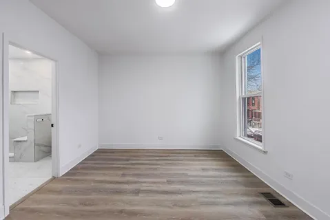 a view of an empty room and bathroom with wooden floor