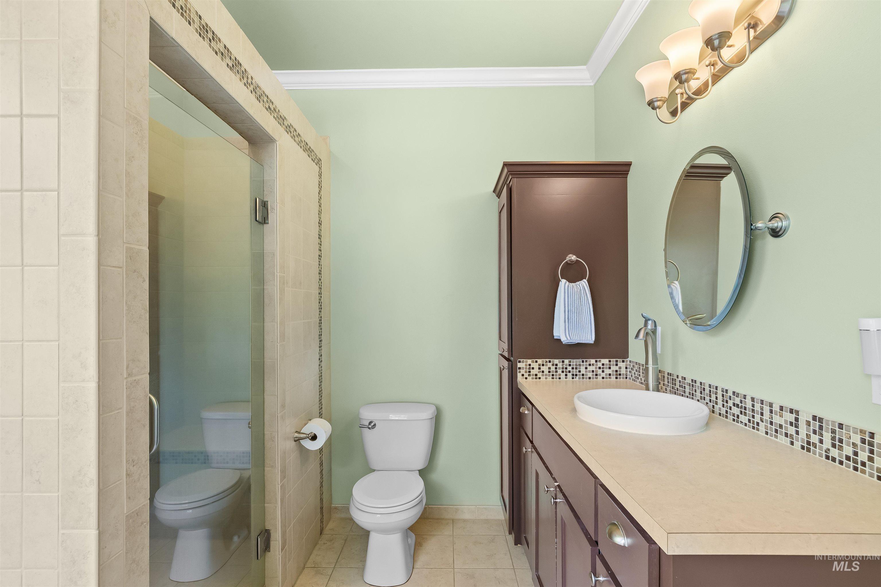 1617 Pine Cone Road Moscow, ID 83843 - Photo 24 of 44 Bathroom featuring a glass-enclosed shower with tile surround, a dark wood-finish vanity with an integrated vessel sink, a light-toned countertop with mosaic tile backsplash, and a wall-mounted oval mirror