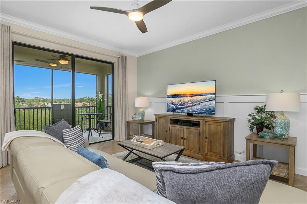 9834 Giaveno Circle, Unit 1746 Naples, FL 34113 - Photo 2 of 41 a living room with furniture a flat screen tv and a floor to ceiling window