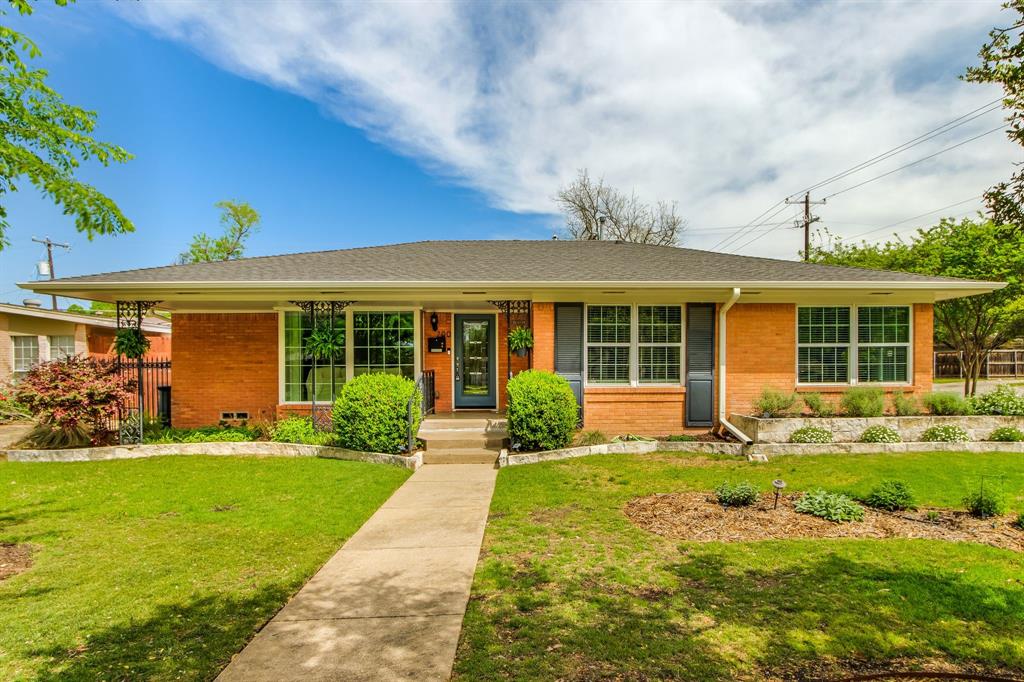 A classic brick ranch-style home features large windows with decorative black iron screens and shutters, framed by well-maintained landscaping and concrete steps leading to the front door.