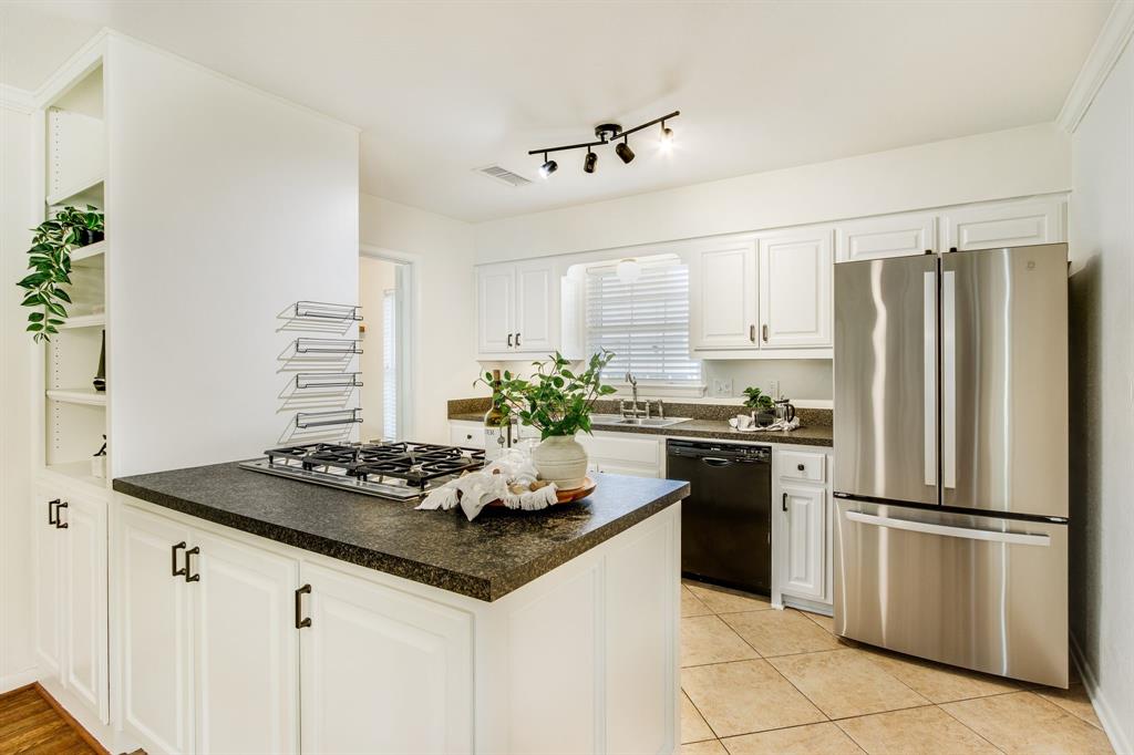 700 Ridgedale Drive Richardson, TX 75080 - Photo 14 of 32 This bright kitchen features crisp white cabinetry with black hardware, high-end stainless steel double ovens, and a built-in gas cooktop set against durable speckled countertops and neutral tile flooring.