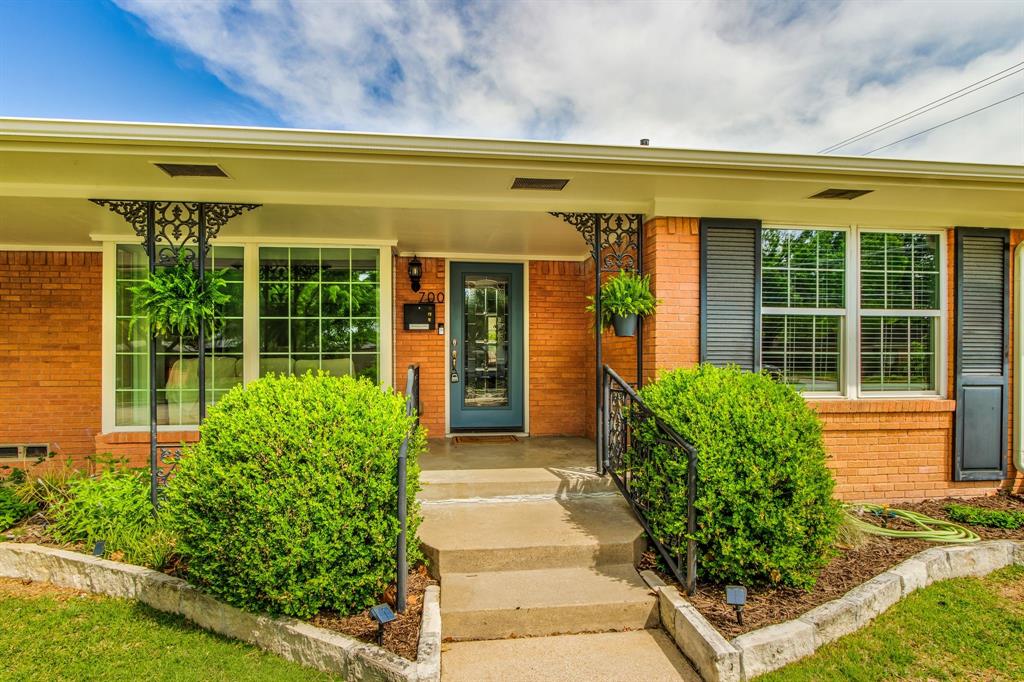 700 Ridgedale Drive Richardson, TX 75080 - Photo 5 of 32 A classic brick ranch-style home features large windows with decorative black iron screens and shutters, framed by well-maintained landscaping and concrete steps leading to the front door.