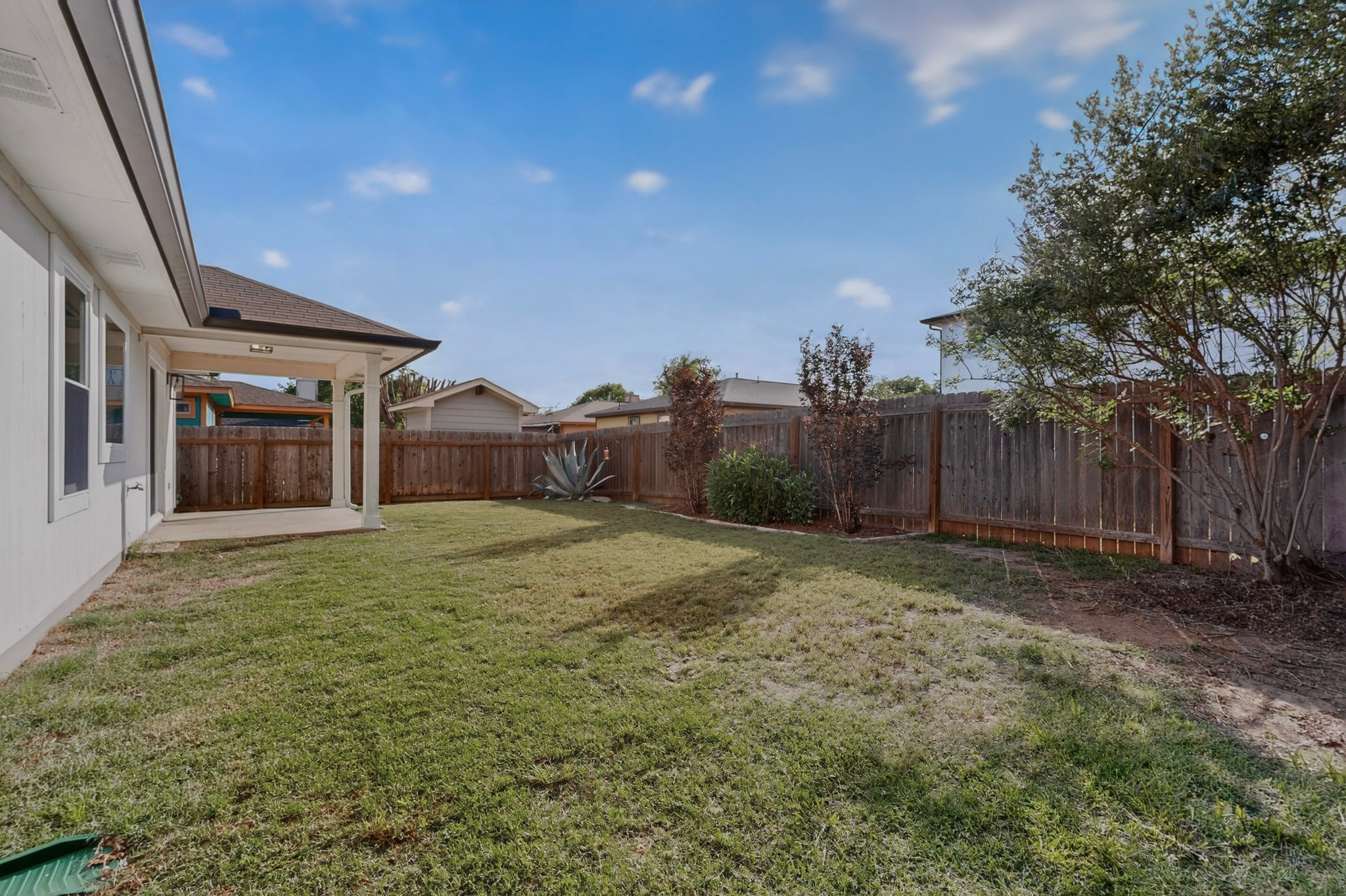 3906 Reeders Drive Austin, TX 78725 - Photo 36 of 36 Expansive backyard featuring a covered patio, wood privacy fencing, a manicured lawn, and established trees and shrubs