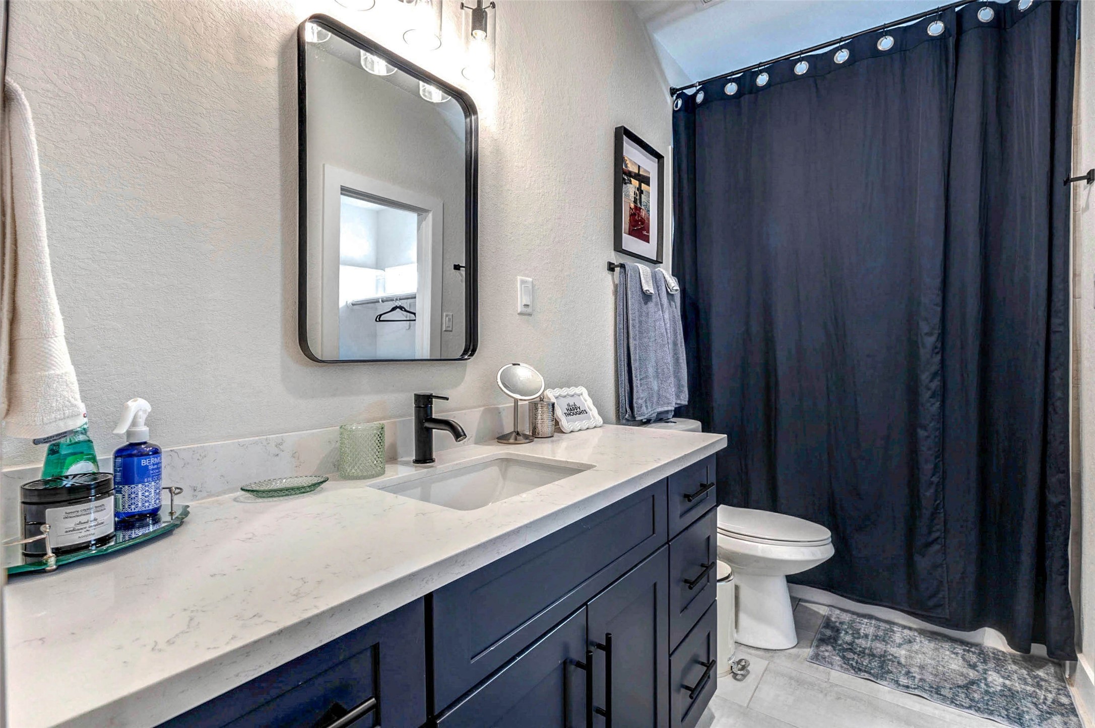 5407 Lee Street Houston, TX 77020 - Photo 12 of 17 This bathroom features a modern design with a sleek dark vanity, white countertop, and stylish black fixtures. It includes a large mirror, ample storage, and a shower with a dark curtain, creating a contemporary and functional space.