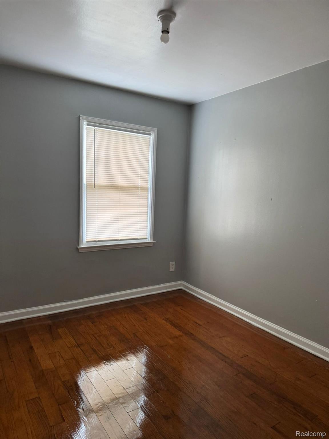 19706 Moross Road Detroit, MI 48224 - Photo 10 of 13 Hardwood flooring, neutral gray wall paint, white trim, window with blinds, and ceiling light fixture