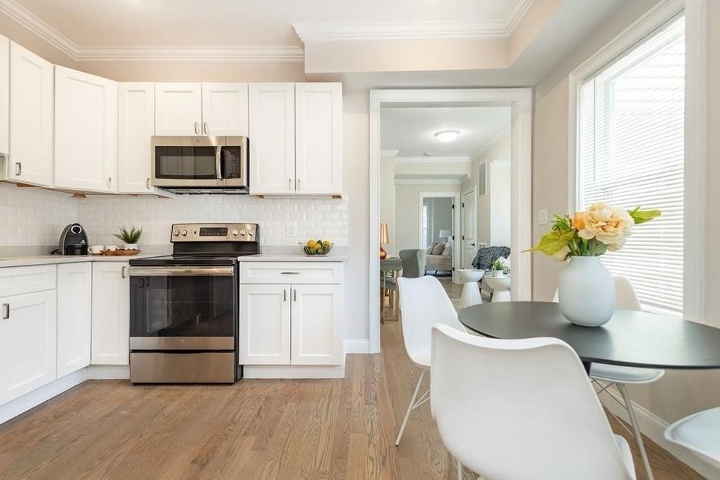 a kitchen with a microwave a stove white cabinets a dining table and chairs