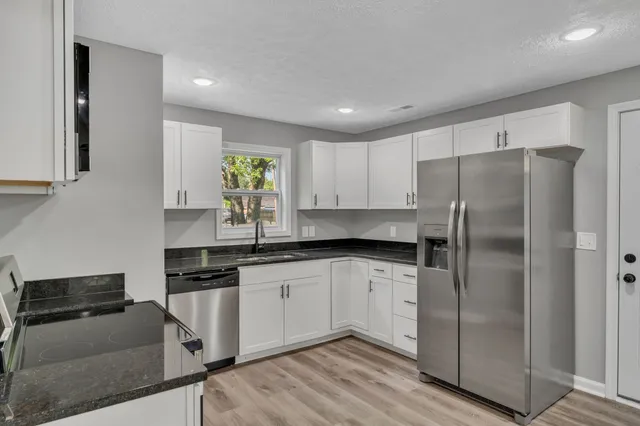 a kitchen with stainless steel appliances granite countertop a refrigerator a sink and white cabinets