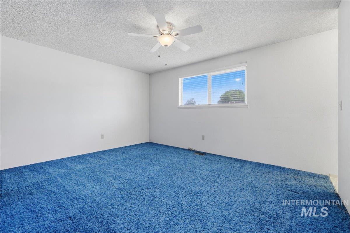 1311 North Middleton Road Nampa, ID 83651 - Photo 24 of 49 Spacious room with vibrant blue carpet, white walls, a multi-pane window with horizontal blinds, and a ceiling fan with integrated lighting