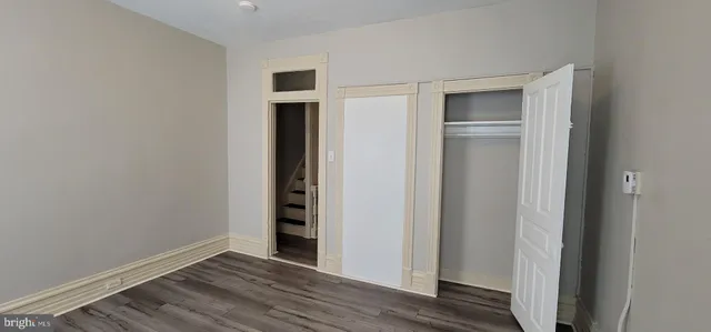 an empty room with wooden floor closet and windows