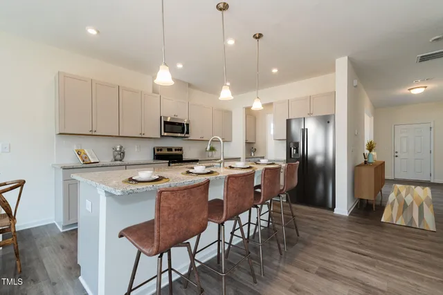 a kitchen with stainless steel appliances granite countertop a sink a stove a refrigerator and a dining table with wooden floor