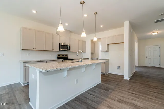 a kitchen with stainless steel appliances granite countertop a sink a stove a refrigerator and white cabinets with wooden floor