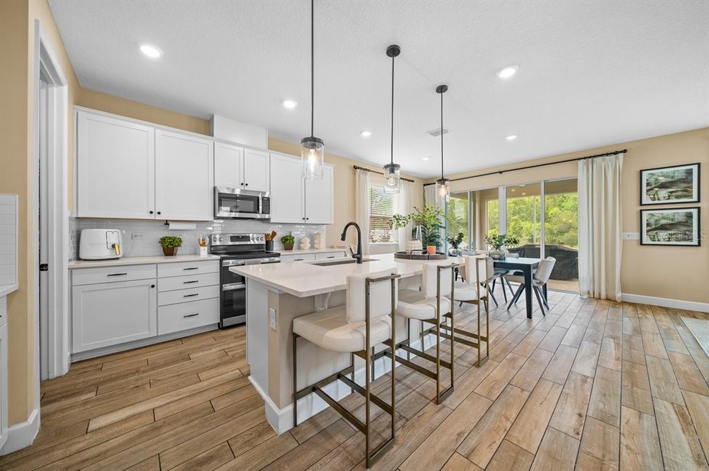 3916 Southern Vista Loop St. Cloud, FL 34772 - Photo 5 of 50 a kitchen with stainless steel appliances kitchen island granite countertop a stove a refrigerator a microwave oven a dining table and chairs with wooden floor