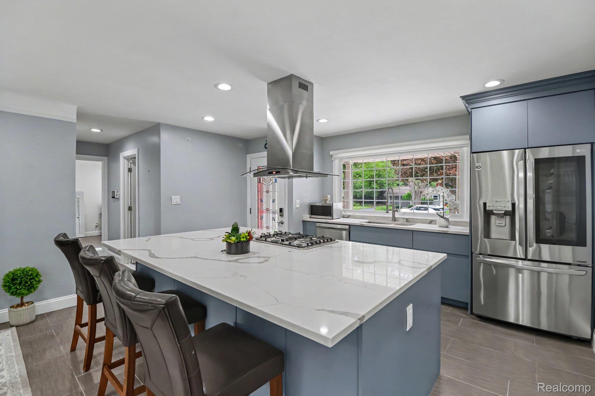 Spacious kitchen featuring a large island with a cooktop, stone-finish countertops, stainless steel appliances, and recessed lighting