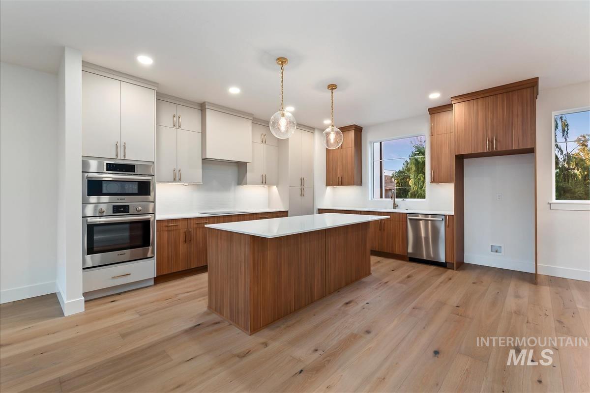 3213 West Moore Street Boise, ID 83702 - Photo 10 of 32 Gourmet kitchen featuring a central island with a white countertop, wood-finish flooring, stainless steel double ovens, and mixed-tone cabinetry