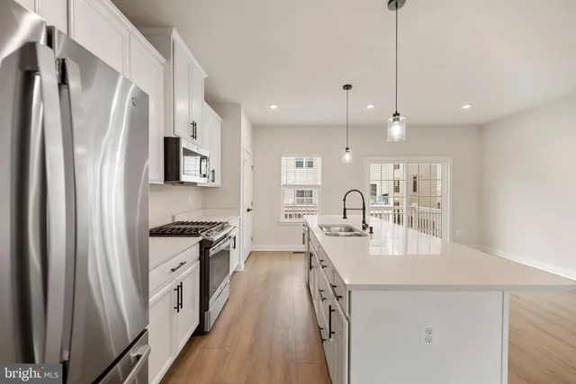 a kitchen with stainless steel appliances granite countertop a refrigerator a sink dishwasher a stove and white countertops with wooden floor