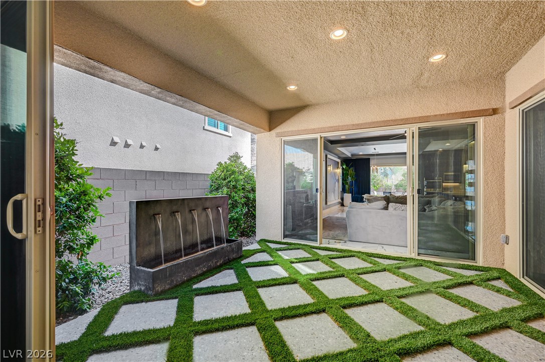 3943 Reyes Avenue Las Vegas, NV 89141 - Photo 51 of 95 An inviting outdoor living space features a tranquil fountain, lush greenery, and patterned pavers leading to large sliding glass doors.