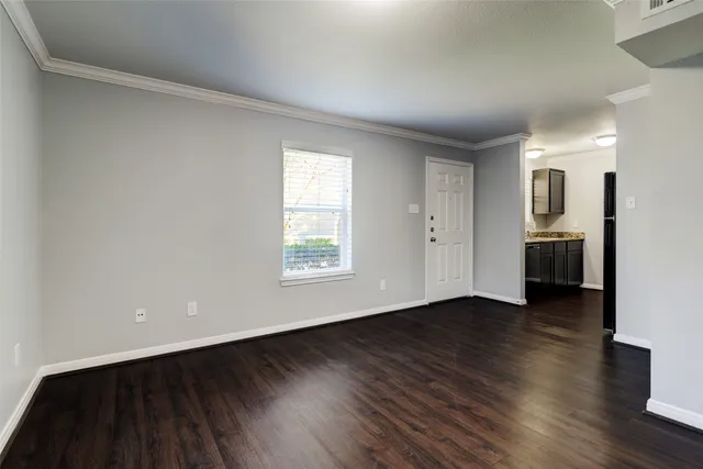 an empty room with wooden floor kitchen view and windows