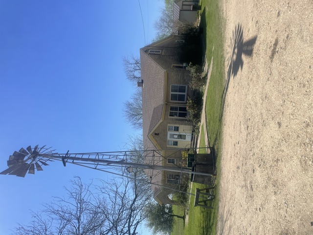 12610 Pecan School Road Bartlett, TX 76511 - Photo 4 of 21 A charming residence with a windmill, set against a clear blue sky, offers peaceful living.