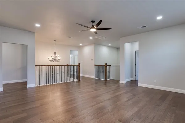 a view of an empty room with wooden floor and a ceiling fan