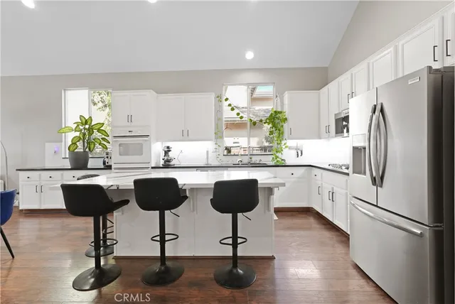 a kitchen with stainless steel appliances kitchen island granite countertop a refrigerator a stove a sink and chairs with wooden floor