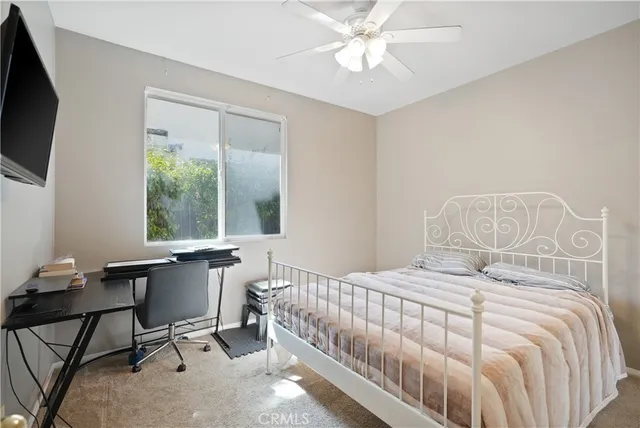 a bedroom with a bed a large window and a flat tv screen on the dresser