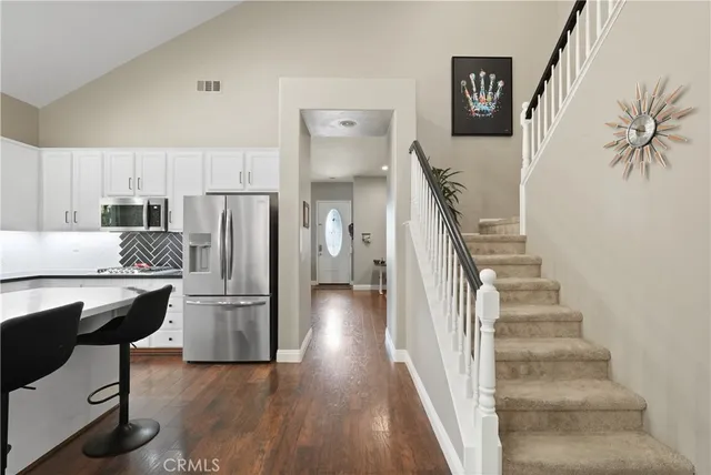 a kitchen with granite countertop a refrigerator a stove and white cabinets with wooden floor