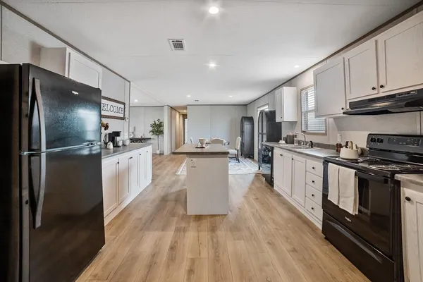 a large kitchen with stainless steel appliances kitchen island granite countertop a refrigerator oven a sink dishwasher and white cabinets with wooden floor