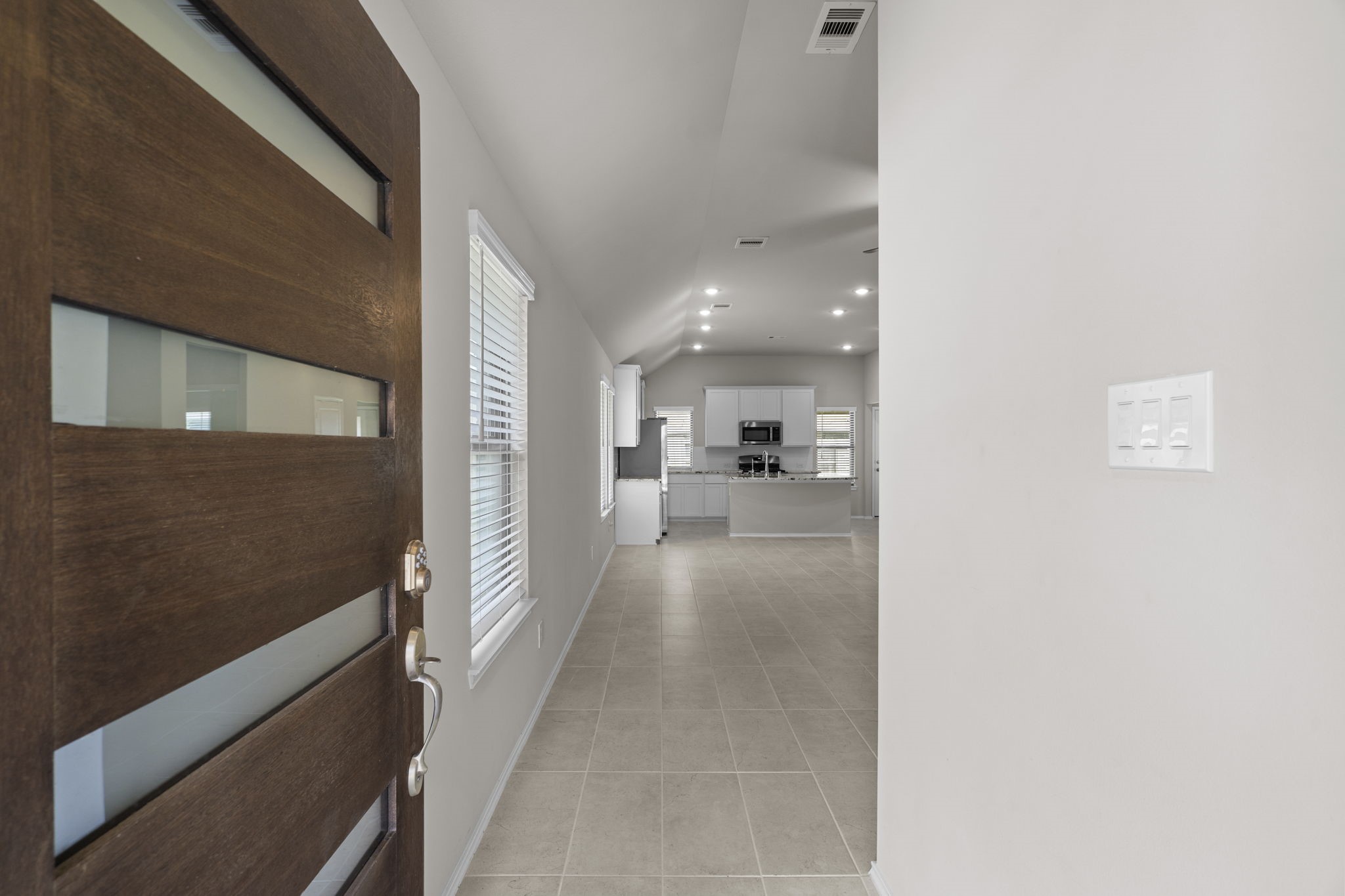 2011 Oak Leaf Court Manvel, TX 77578 - Photo 5 of 28 Modern entryway with a sleek wooden door leading into an open-plan space. The interior features neutral tiles, recessed lighting, and a glimpse of a contemporary kitchen with white cabinetry and stainless-steel appliances.