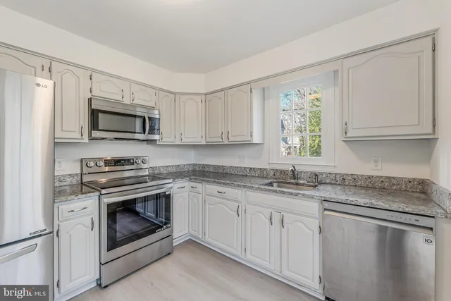 a kitchen with granite countertop white cabinets white stainless steel appliances a sink and a window