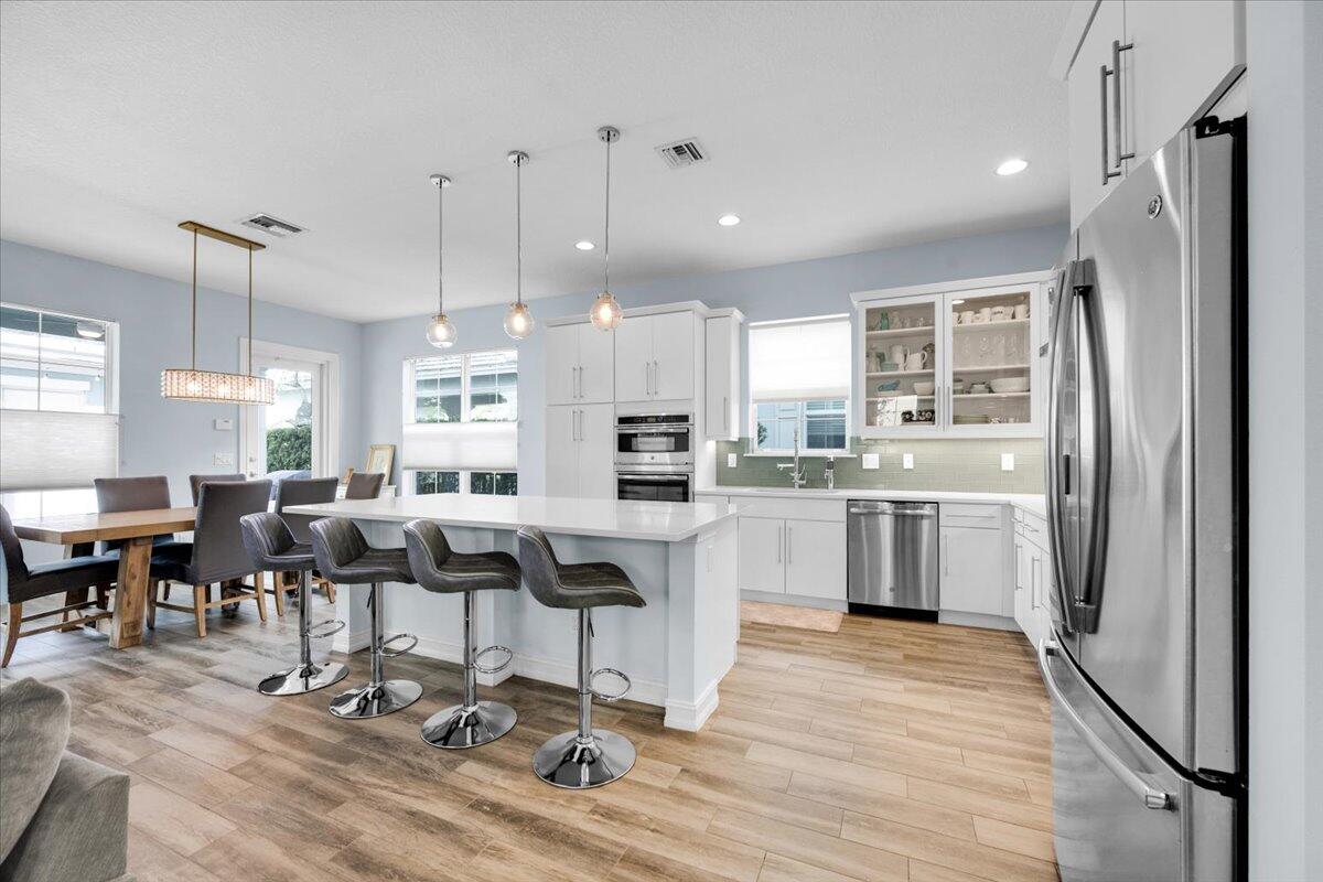 120 West Bay Cedar Circle Jupiter, FL 33458 - Photo 9 of 33 a kitchen with stainless steel appliances kitchen island granite countertop a refrigerator a stove a sink and chairs with wooden floor