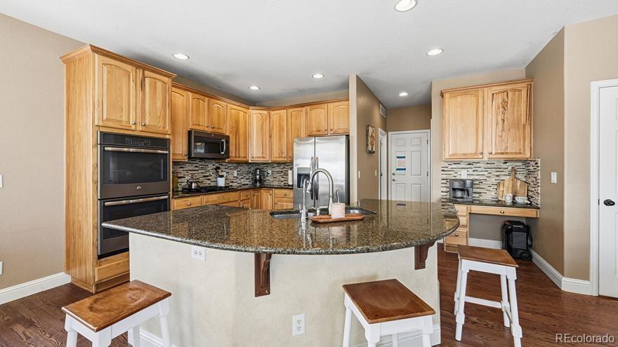 7869 Solstice Way Castle Rock, CO 80108 - Photo 14 of 41 a kitchen with kitchen island granite countertop a stove a refrigerator a sink and white cabinets with wooden floor