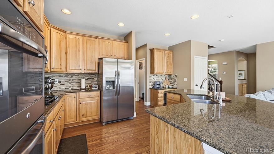 7869 Solstice Way Castle Rock, CO 80108 - Photo 15 of 41 a kitchen with stainless steel appliances granite countertop a refrigerator a stove and a sink with wooden floor