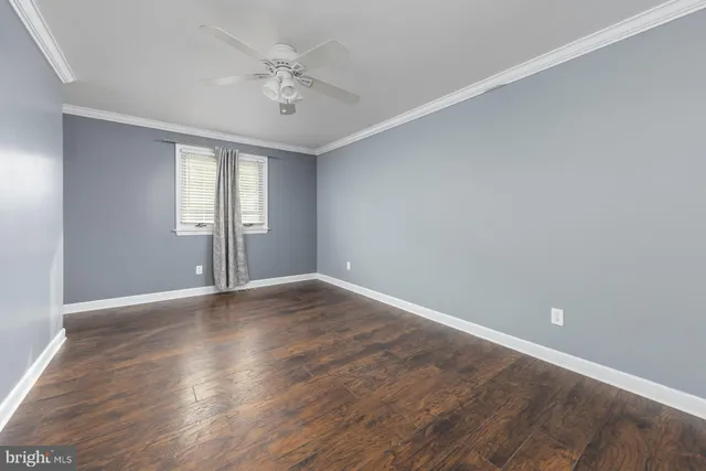 a view of an empty room with wooden floor and a ceiling fan