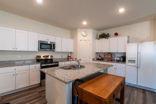 a kitchen with granite countertop a stove top oven a sink dishwasher a refrigerator and cabinets with wooden floor