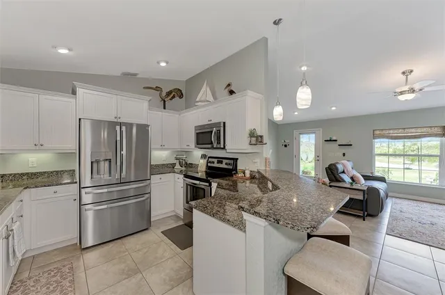 a kitchen with granite countertop kitchen island stainless steel appliances a refrigerator a stove a sink a dining table and chairs with wooden floor