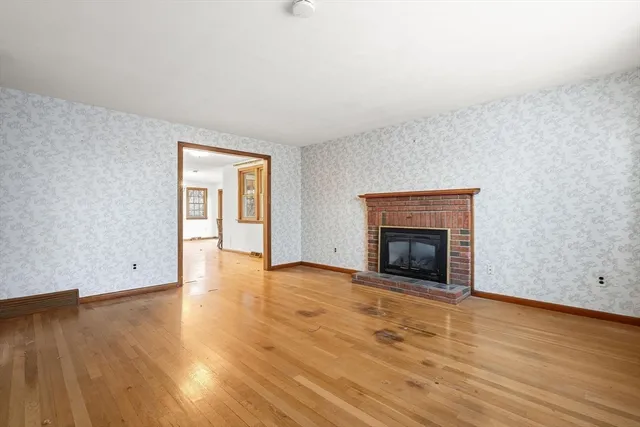 a view of an empty room with wooden floor fireplace and a window