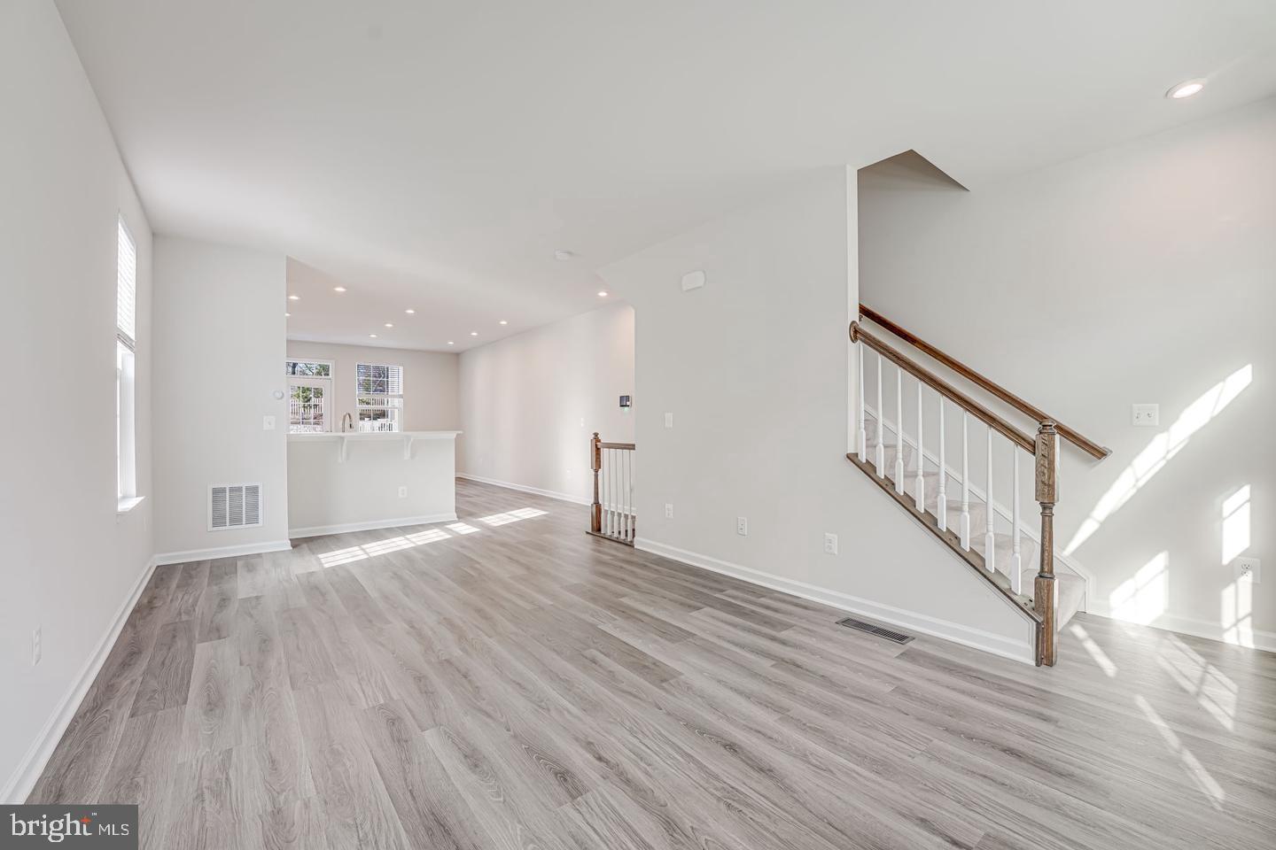 a view of an empty room with wooden floor and a kitchen