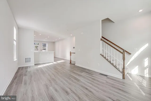 a view of an empty room with wooden floor and a kitchen