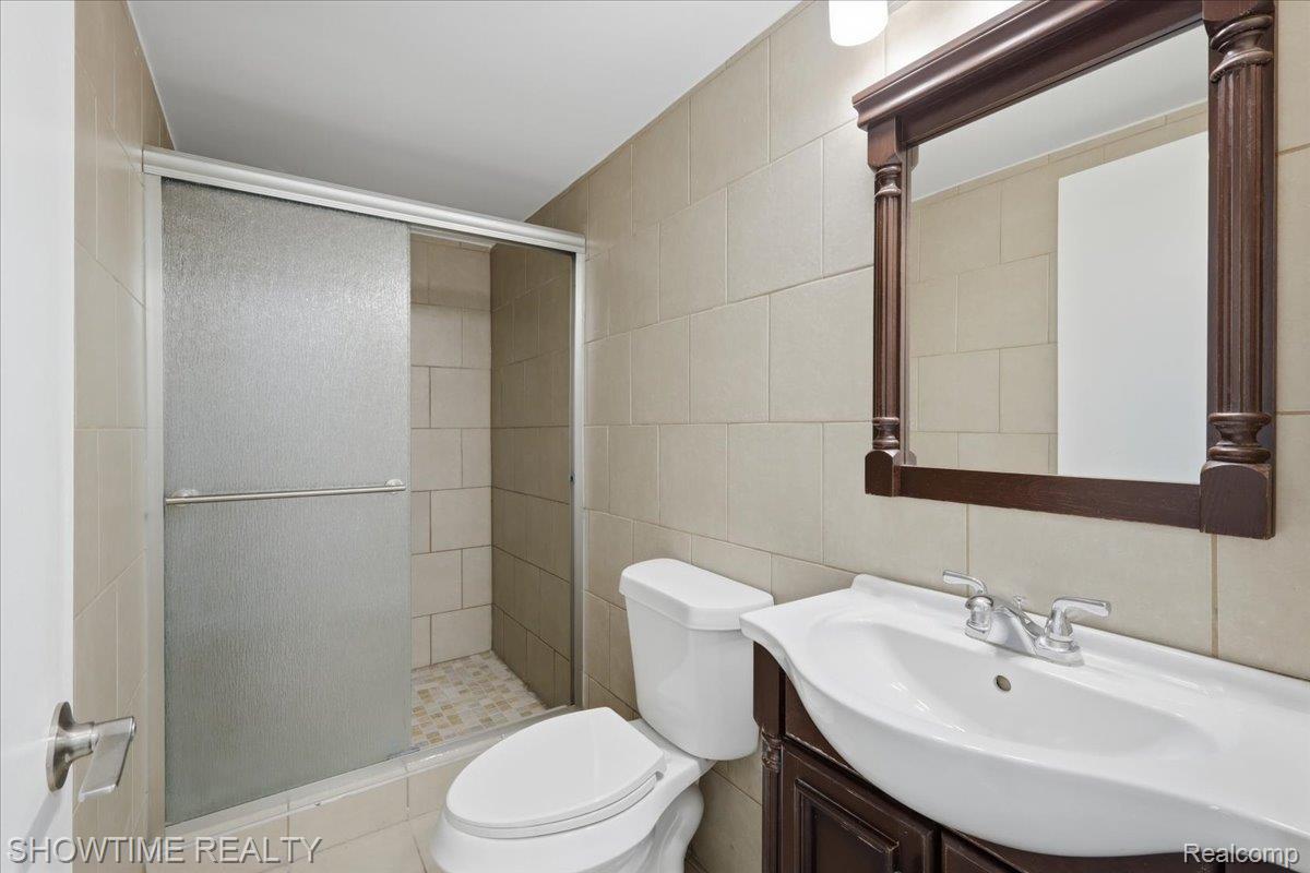 29255 Utley Road Farmington, MI 48334 - Photo 22 of 46 Bathroom featuring a shower with sliding glass doors, a vanity with a white basin sink, a dark wood-finish vanity cabinet, and a framed mirror