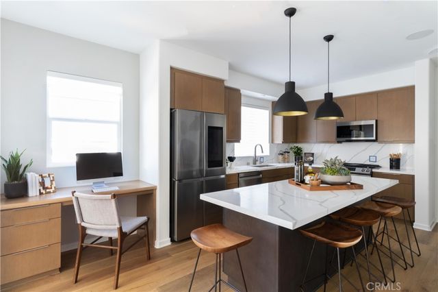 a open kitchen with stainless steel appliances granite countertop a sink a stove a refrigerator a dining table and chairs with wooden floor