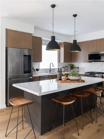 a kitchen with stainless steel appliances a sink a stove a refrigerator and chairs