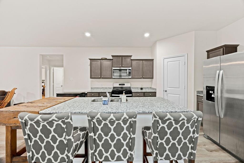 822 Ramble Road Lavon, TX 75166 - Photo 11 of 35 Kitchen featuring a large central island with granite countertop, stainless steel appliances, modern cabinetry, recessed lighting, and wood-finish flooring